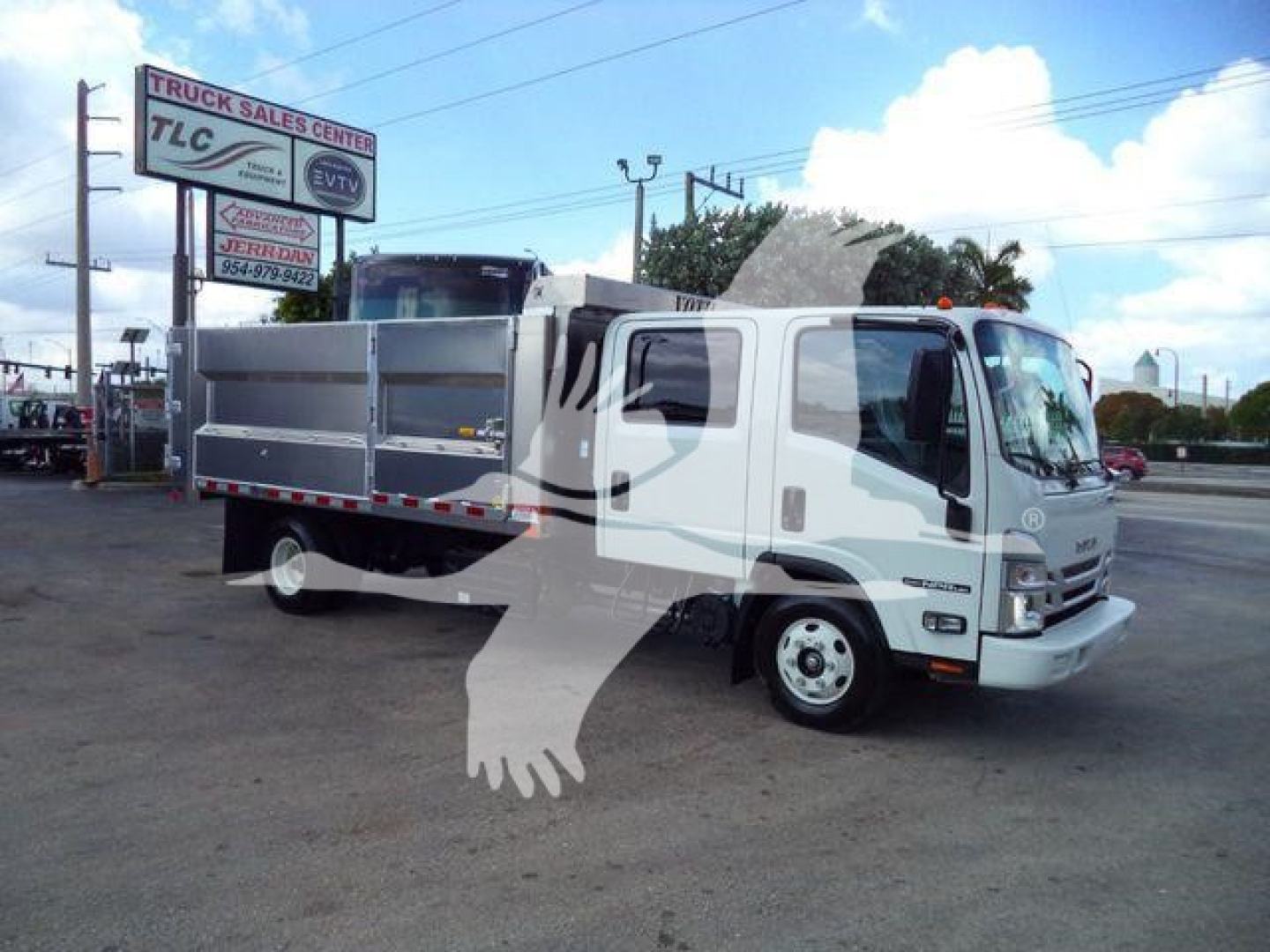 Isuzu NPR-HD dump truck in a dealership lot with silver dump bed, white cab, side mirrors, bumper, and safety decals visible.
