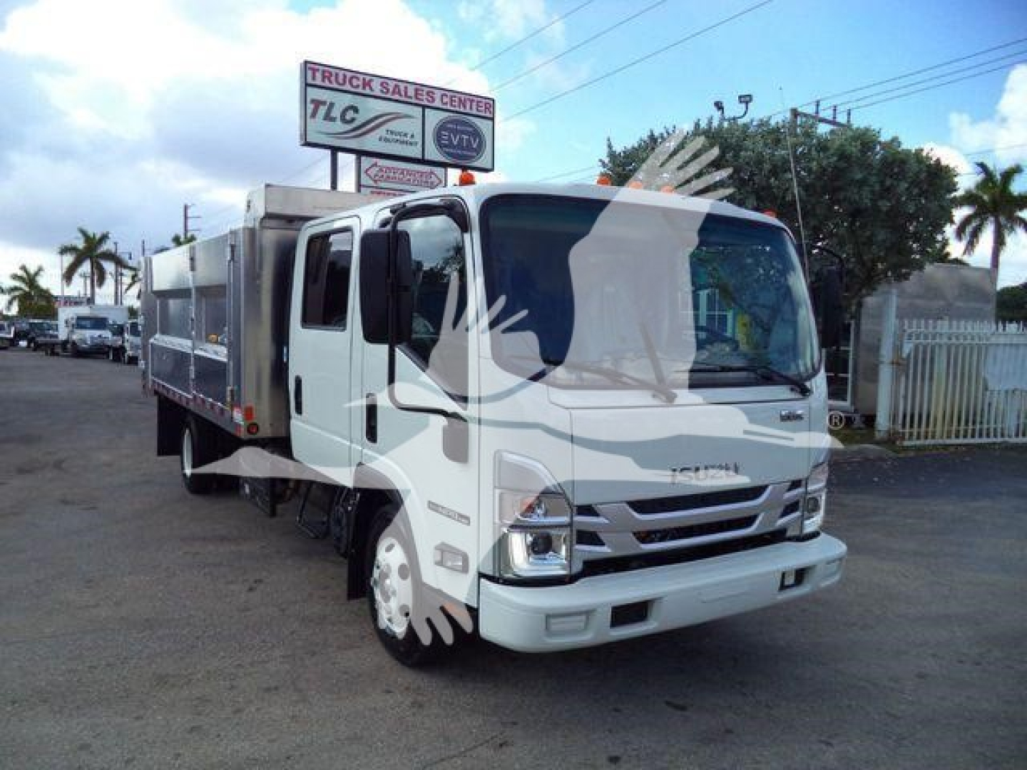 Isuzu NPR HD dump truck in a dealership lot showing front and side with a dump bed. Visible text on dealership sign in background.