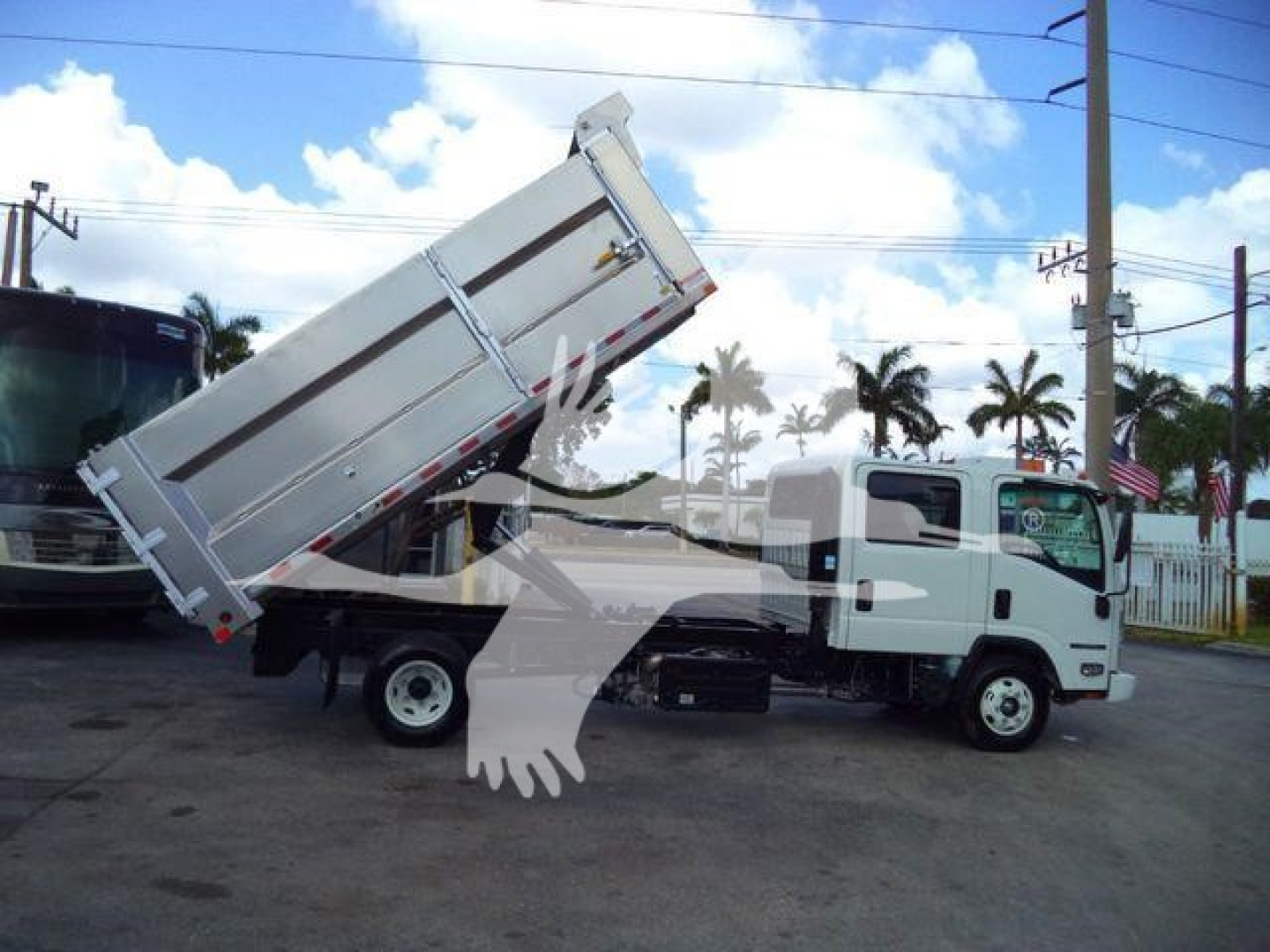 Isuzu NPR-HD dump truck with bed raised on a dealership lot, side view showing dump body and front cab, clear blue sky.