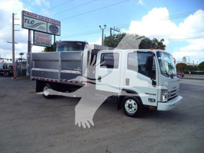Isuzu NPR-HD dump truck in a dealership lot with silver dump bed, white cab, side mirrors, bumper, and safety decals visible.