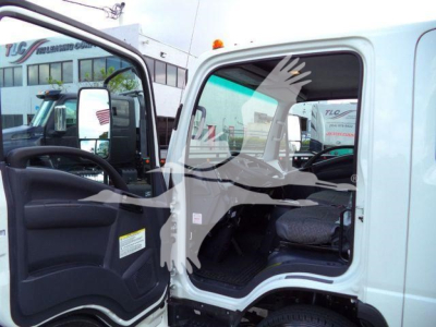 Isuzu NPR HD dump truck cab with open door showing driver seat and interior; faint website sign and building reflected in window.