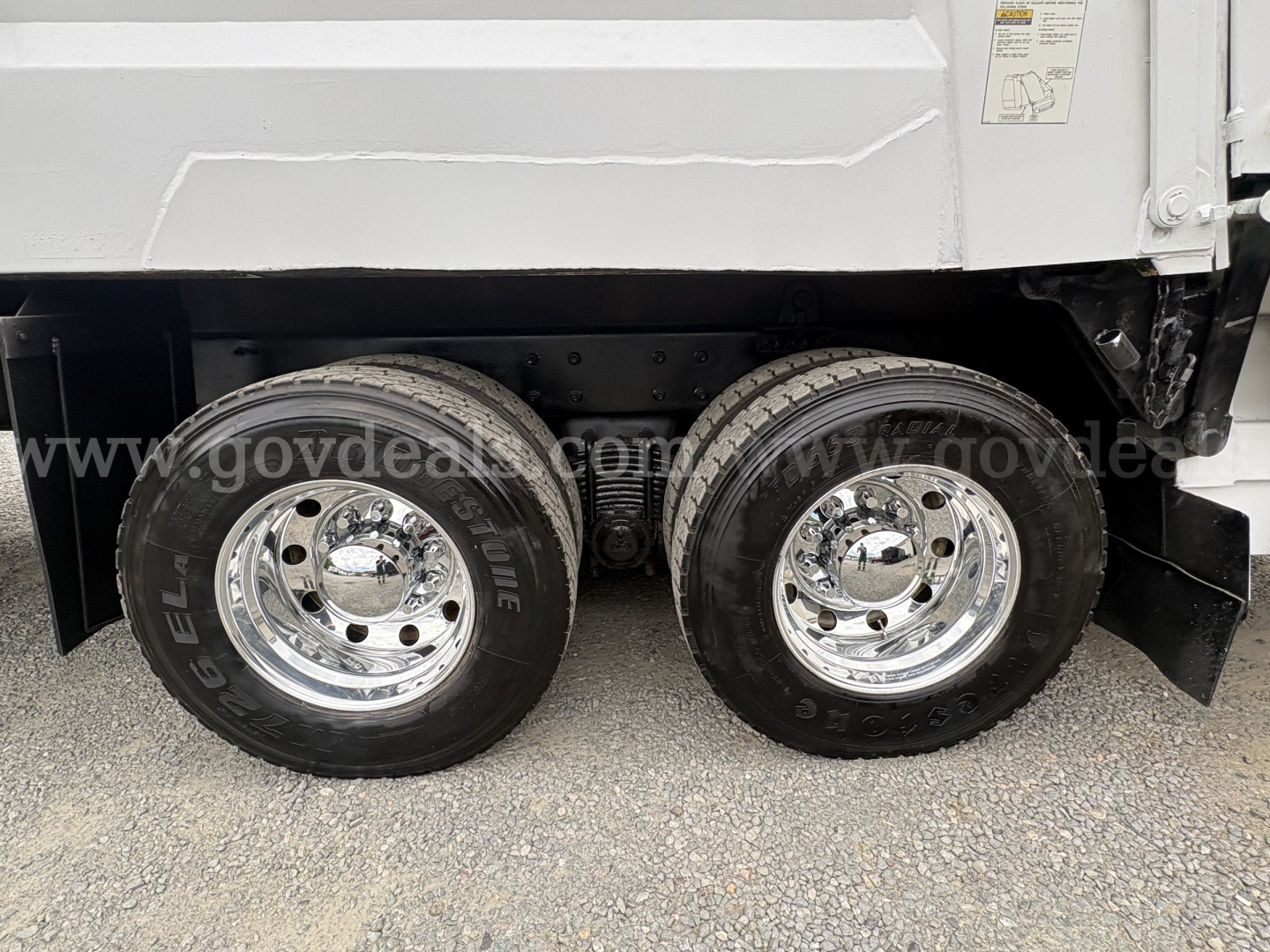 Dual rear wheels of a Mack GU713 dump truck with chrome rims and black tires.