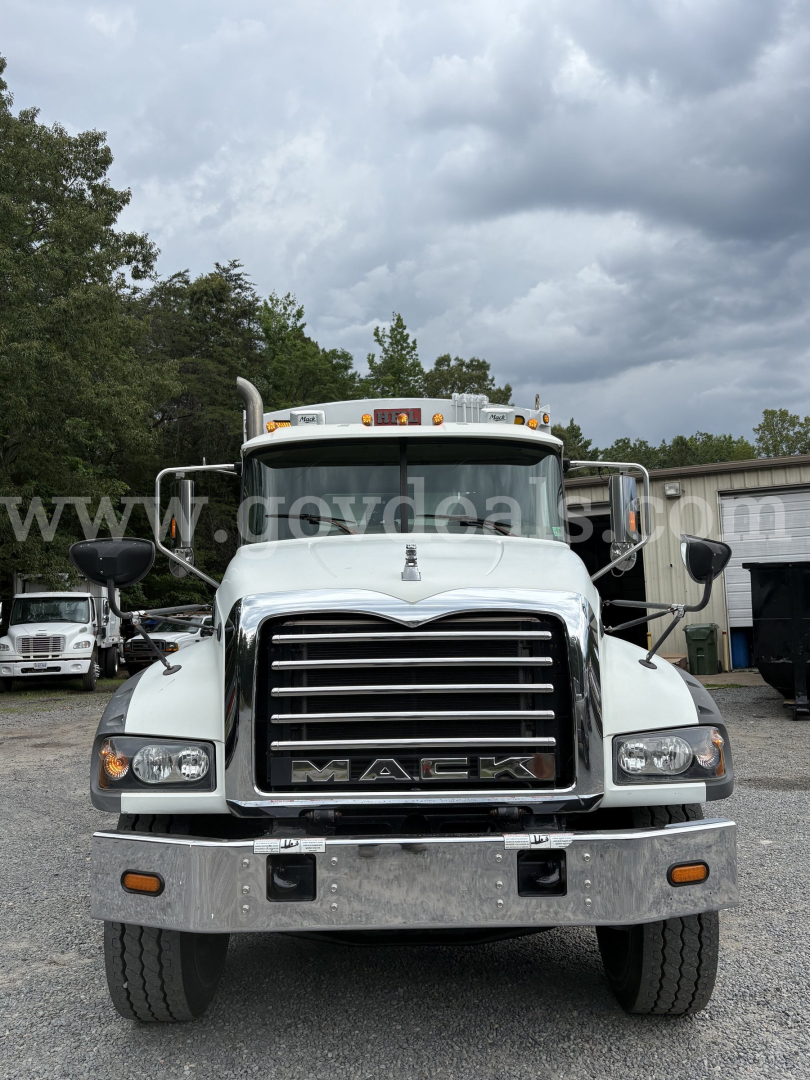 Front view of a white 2015 Mack GU713 truck showing chrome grille with MACK lettering, large bumper, headlights, and side mirrors.