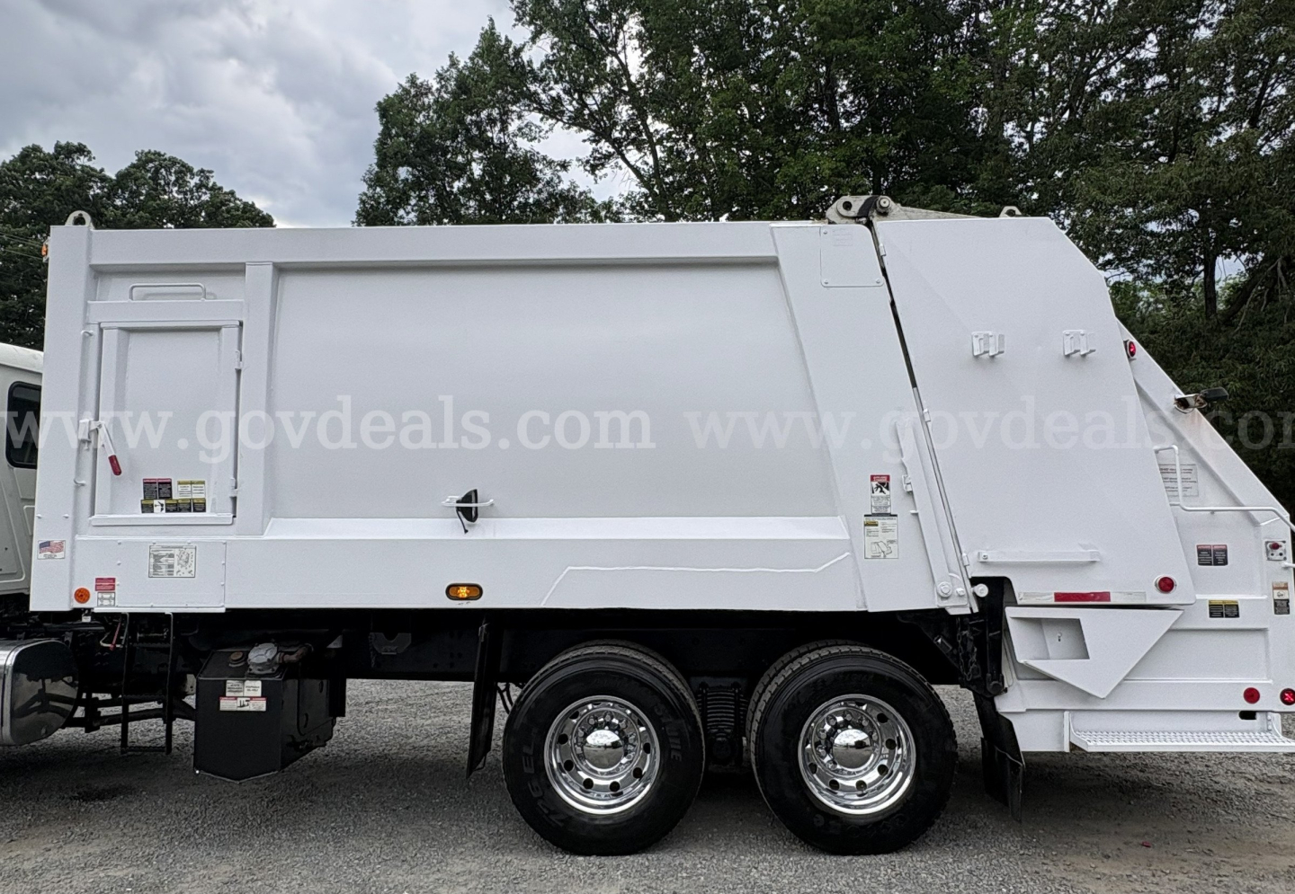 Mack GU713 garbage truck side view showingLarge waste body and dual rear tandem wheels with white exterior.