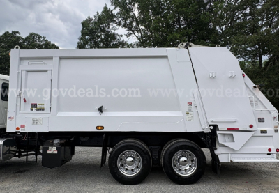 Mack GU713 garbage truck side view showingLarge waste body and dual rear tandem wheels with white exterior.