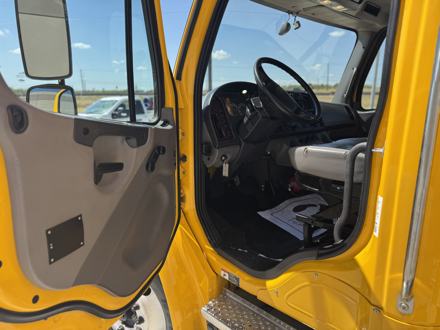 Cab interior of a yellow 2022 Freightliner M2-106 with open door showing steering wheel and dashboard.