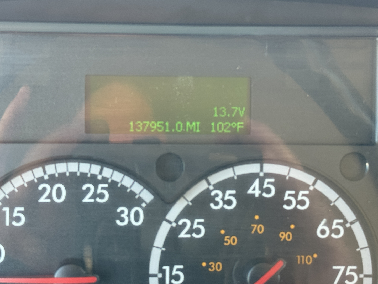 Dashboard display of a Freightliner M2-106 showing digital readout with 137,951.0 miles, 102°F, 13.7V. Analog gauges with speedometer and tachometer.