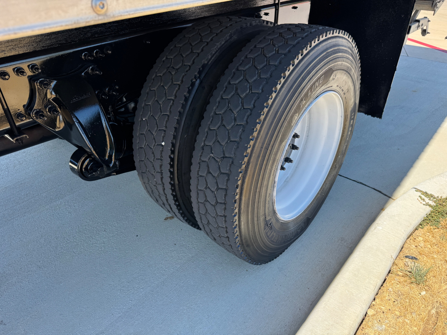 Fleet chassis with dual rear wheels and black frame showing Freightliner M2-106 undercarriage and tire tread.