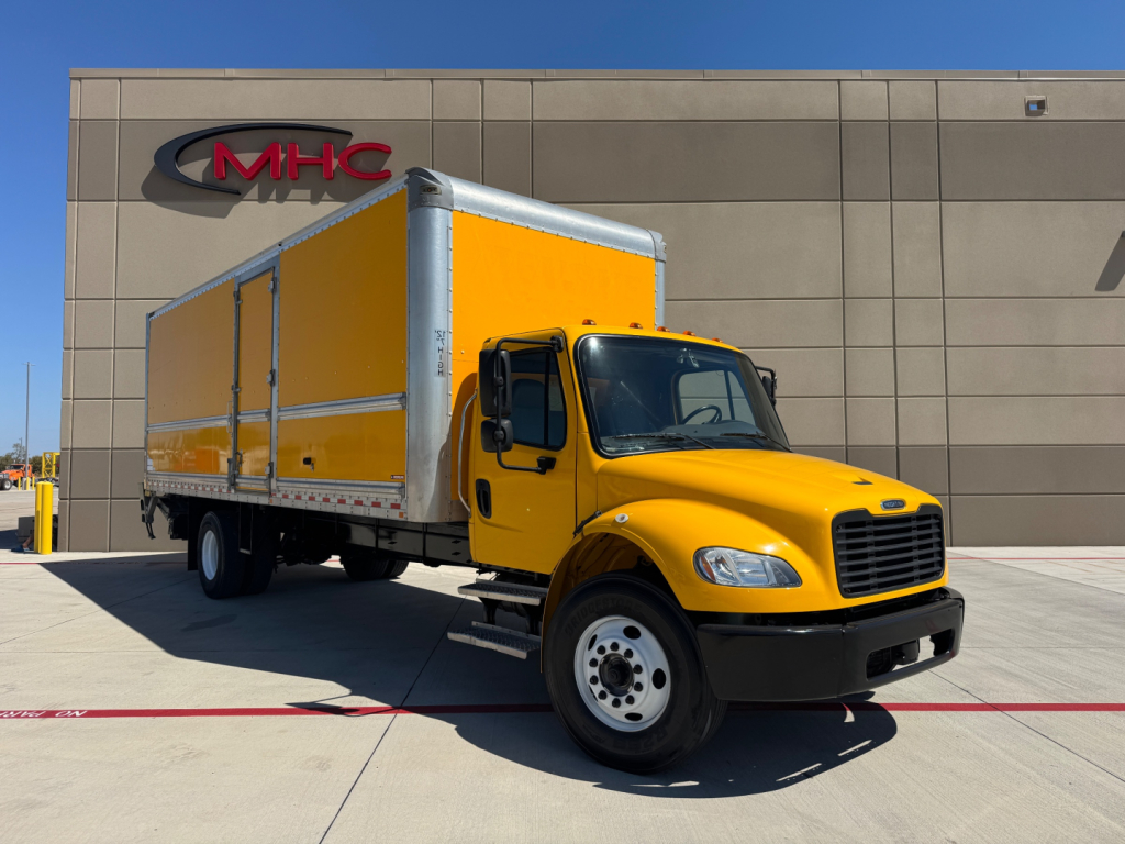 Freightliner M2-106 medium-duty box truck in yellow with cargo box, parked outside a dealership.