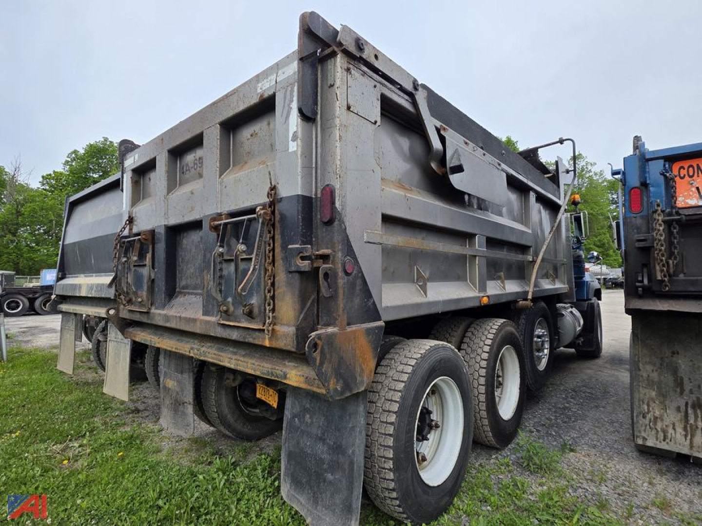 Dump truck rear-side view showing gravel dump bed and triple rear axle on a Mack RD688S. Visible are hydraulic tailgate latches and worn metal surface.