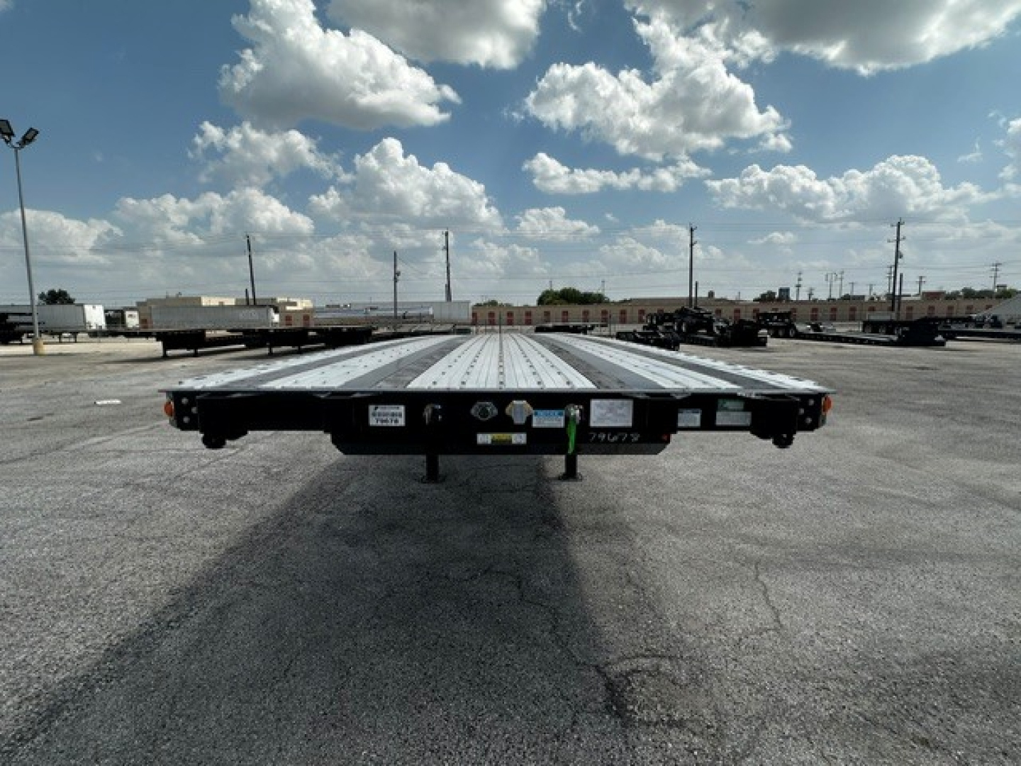 Flatbed trailer viewed from the rear showing a long perforated metal deck with tail lights and support legs.