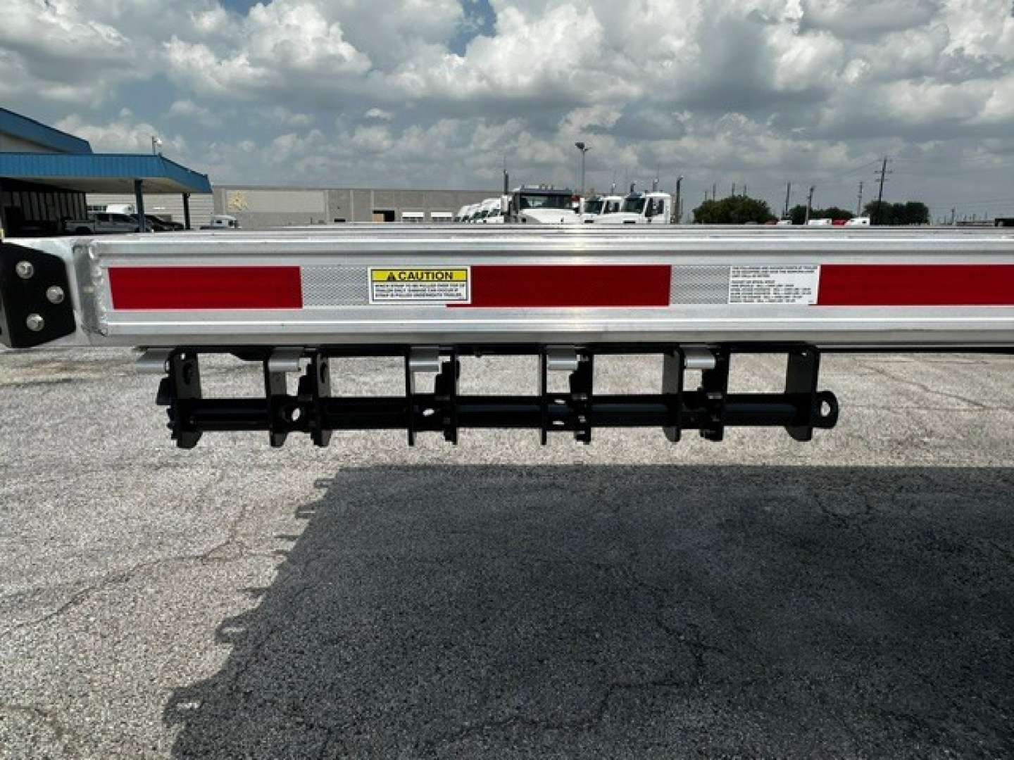 Flatbed trailer tail with reflective red/white tape and rear bumper/ladder rack showing caution label and mounting hardware.