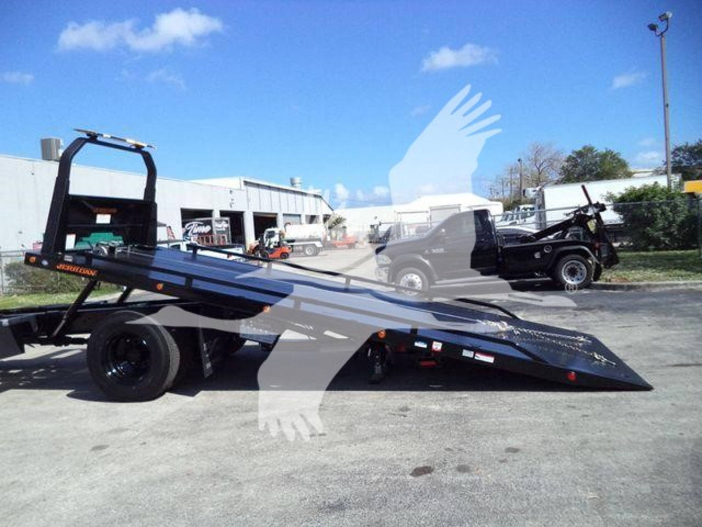 Flatbed rollback tow truck in service position showing low-profile ramp with hydraulic tilt and black chassis.