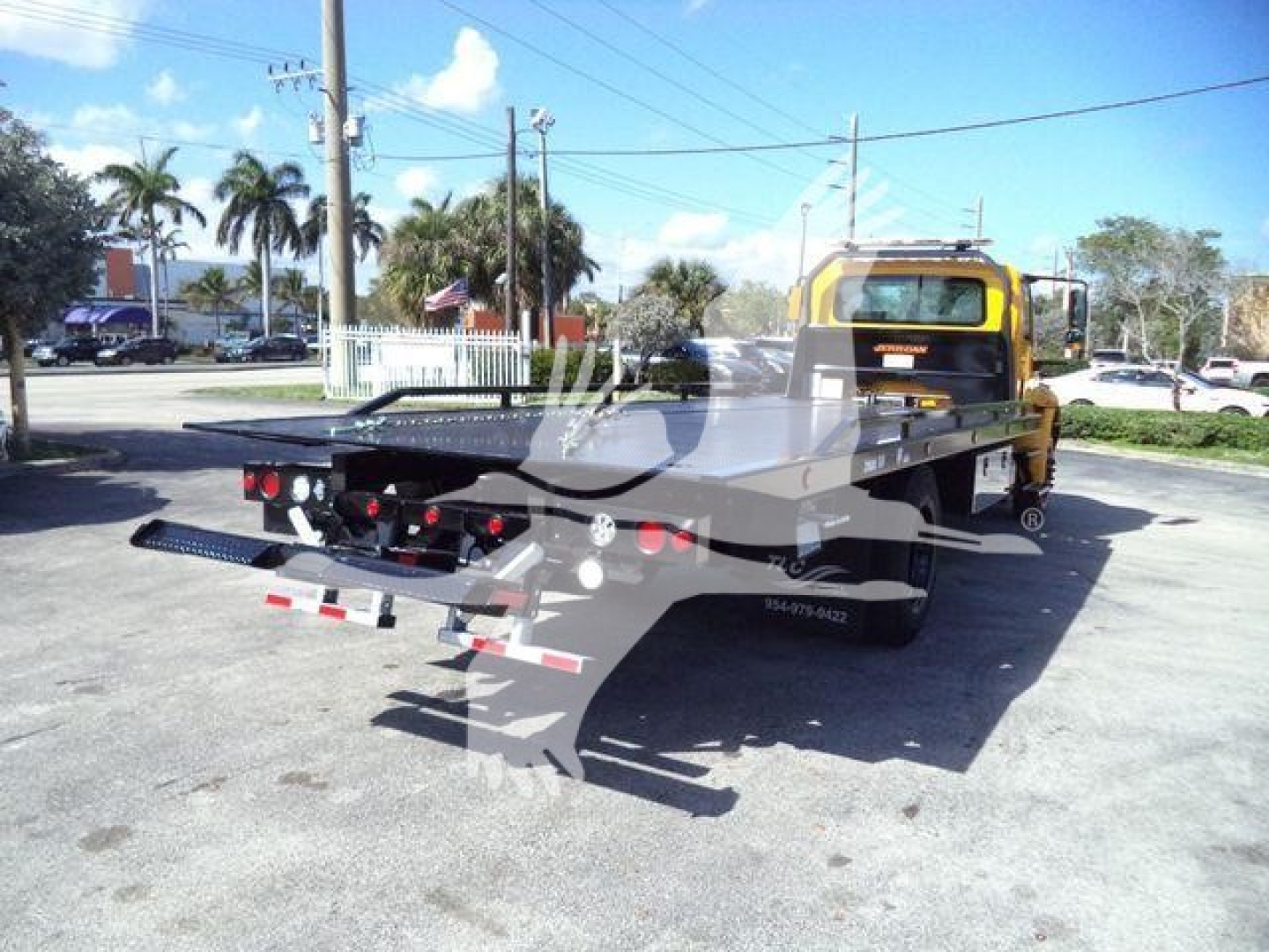 Truck bed tow truck rear view of 2019 International Durastar 4300 rollback with yellow cab and black flatbed viewed from left rear.