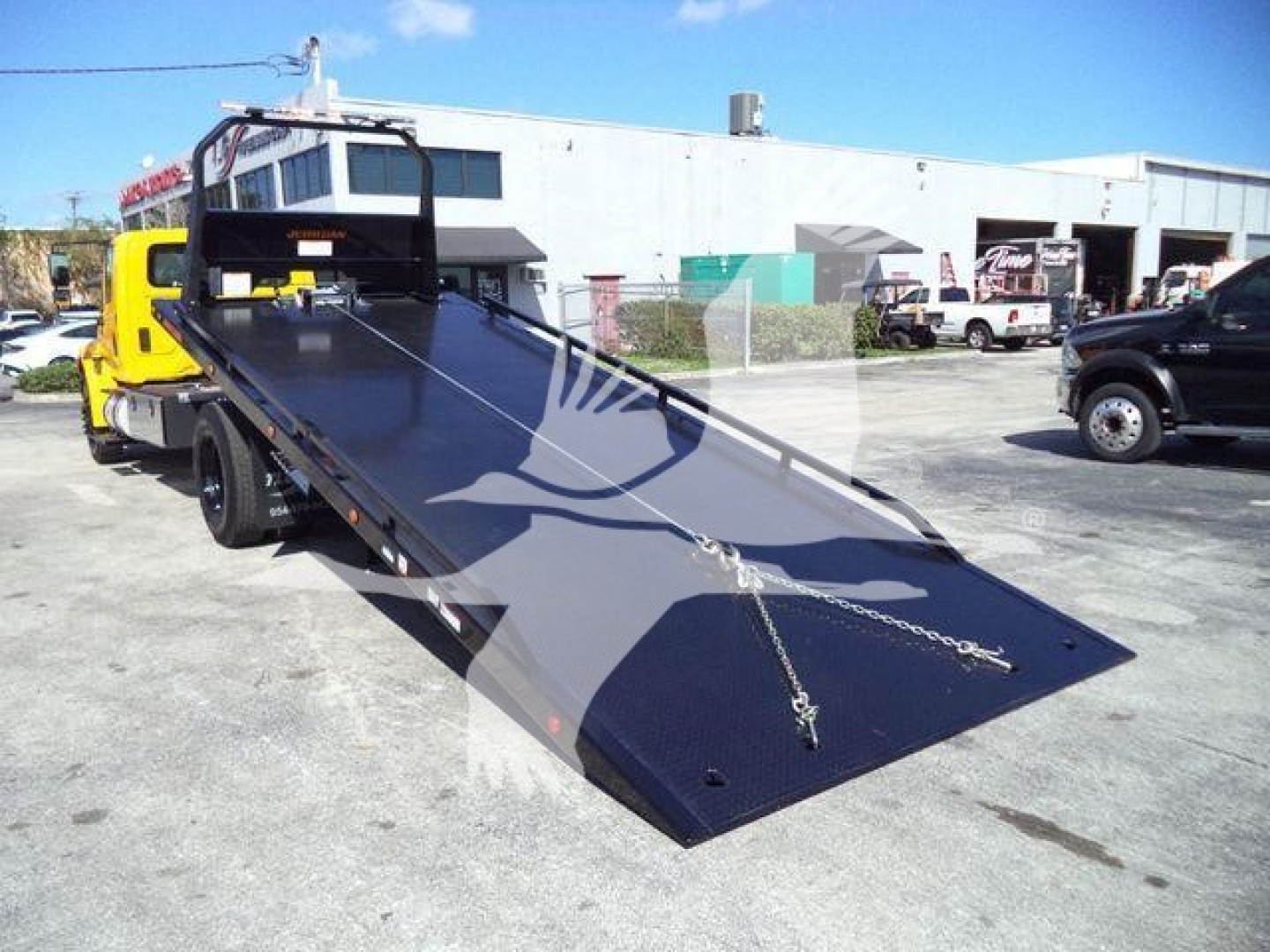 Truck bed with hydraulic rollback tilt on a yellow International Durastar 4300, loading ramp extended in a used equipment lot.