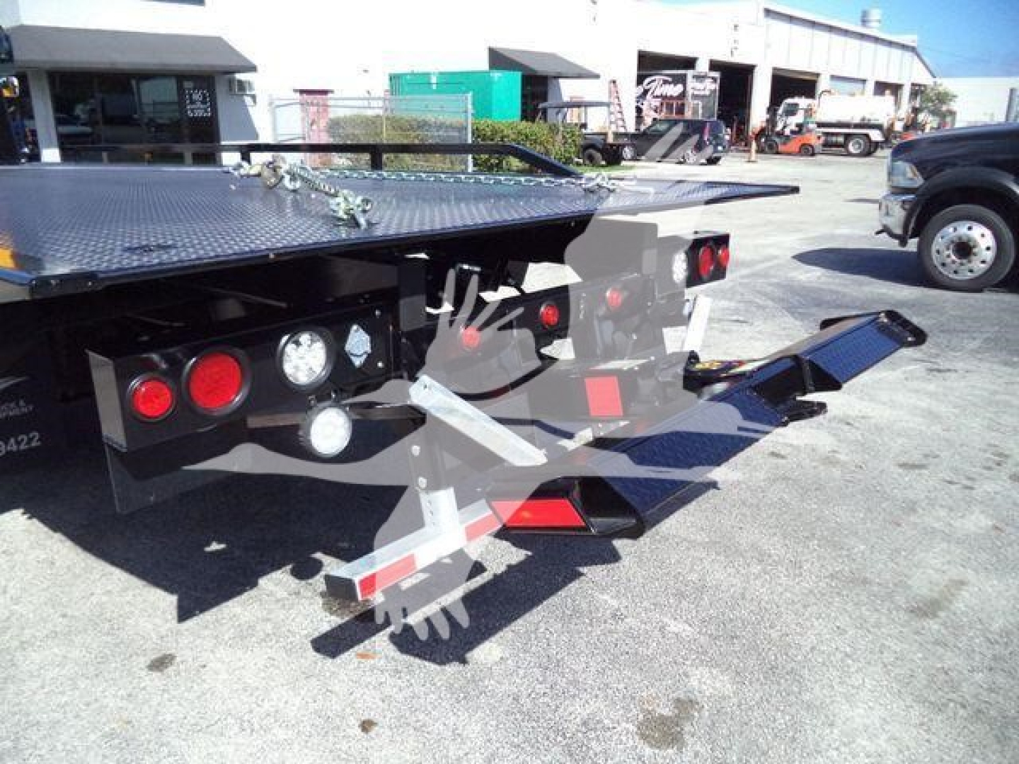 Flatbed tow truck rollback showing rear deck and hydraulic components with taillights and warning reflectors.
