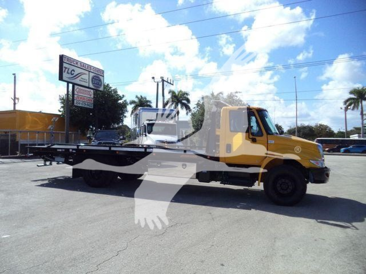 2019 International Durastar 4300 rollback truck in a sale lot with yellow cab and long flatbed.
