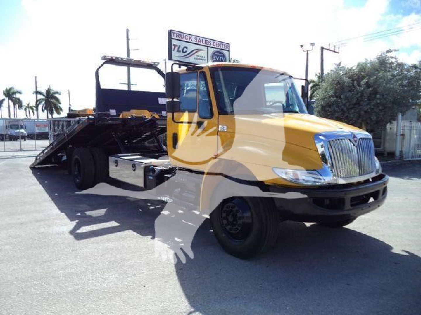 2019 International Durastar 4300 rollback truck with yellow cab, black flatbed, and hydraulic ramps in a dealership lot.