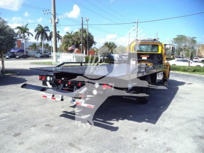 Truck bed tow truck rear view of 2019 International Durastar 4300 rollback with yellow cab and black flatbed viewed from left rear.