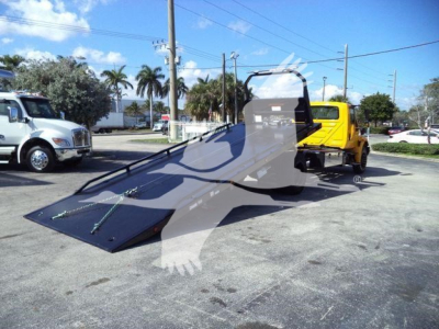 Truck rollback with a yellow cab and a long inclined flatbed ramp, showing a hydraulic winch area and load bed.