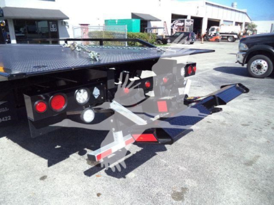 Flatbed tow truck rollback showing rear deck and hydraulic components with taillights and warning reflectors.