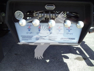Control panel of rollback truck with multiple levers and a gauge, label area showing operating instructions and brand 'Jerr-Dan'