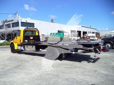 International Durastar 4300 rollback truck with yellow cab and flatbed in a lot.