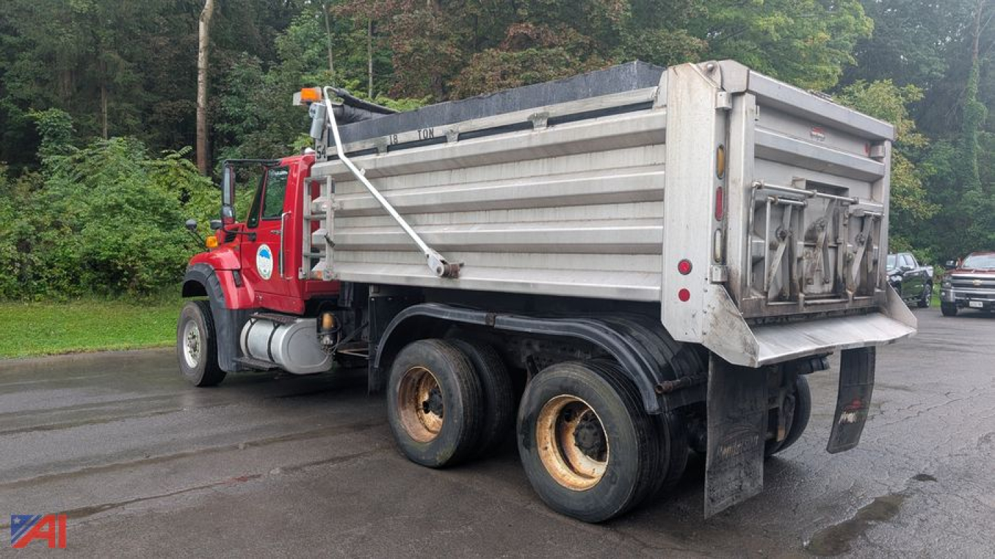 Dump truck rear/side view showing dual rear axles, dump bed, and tailgate with hinges. Door paneling and hydraulic system visible, wheel rims rusted. No readable serials or labels.