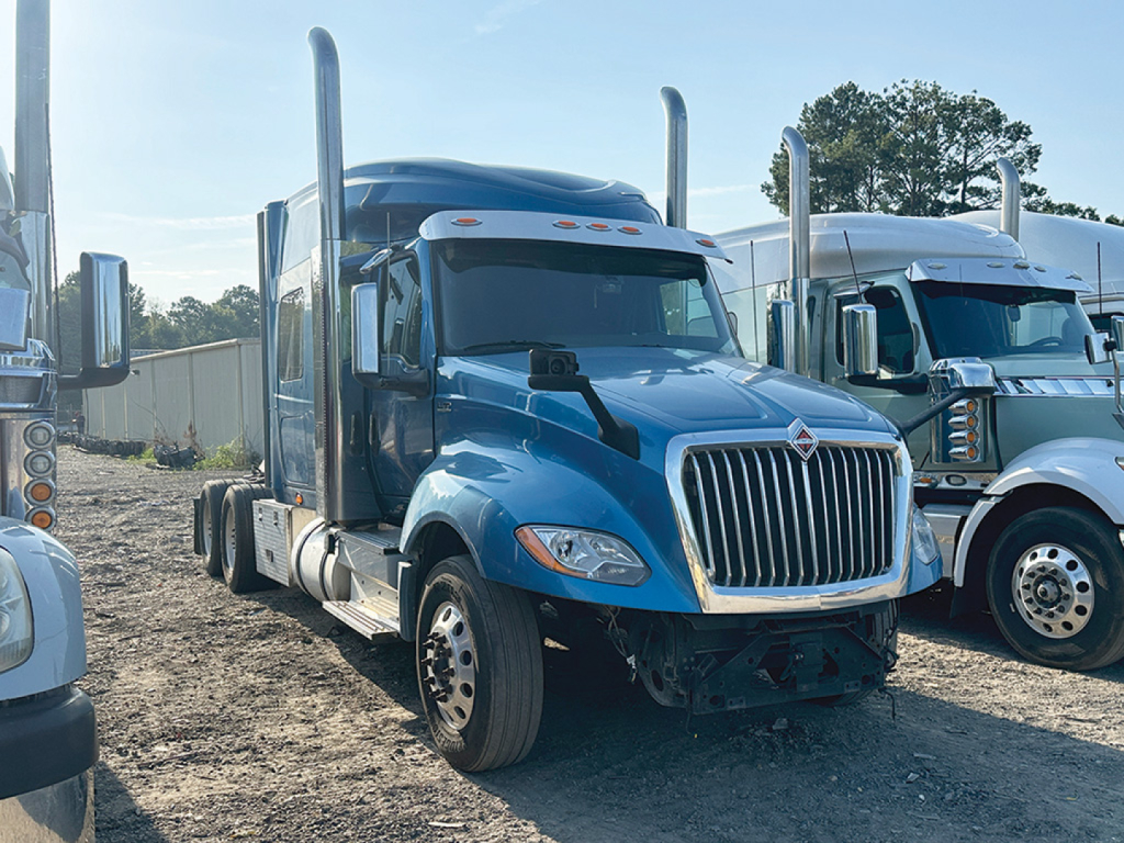 Truck cab showing 2019 International LT625 with blue exterior, front grille, dual vertical exhaust stacks, and side mirrors; cargo tractor in dealership lot.