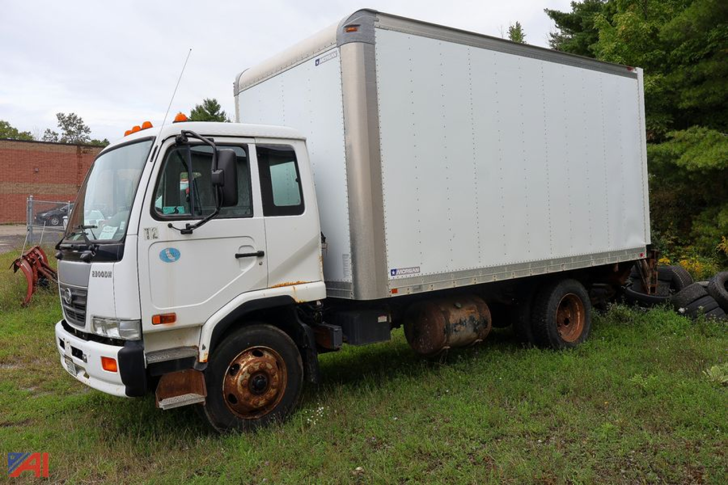Box truck with white cab and large box cargo area, UD cab over engine, front wheels rusted, parked on grass.