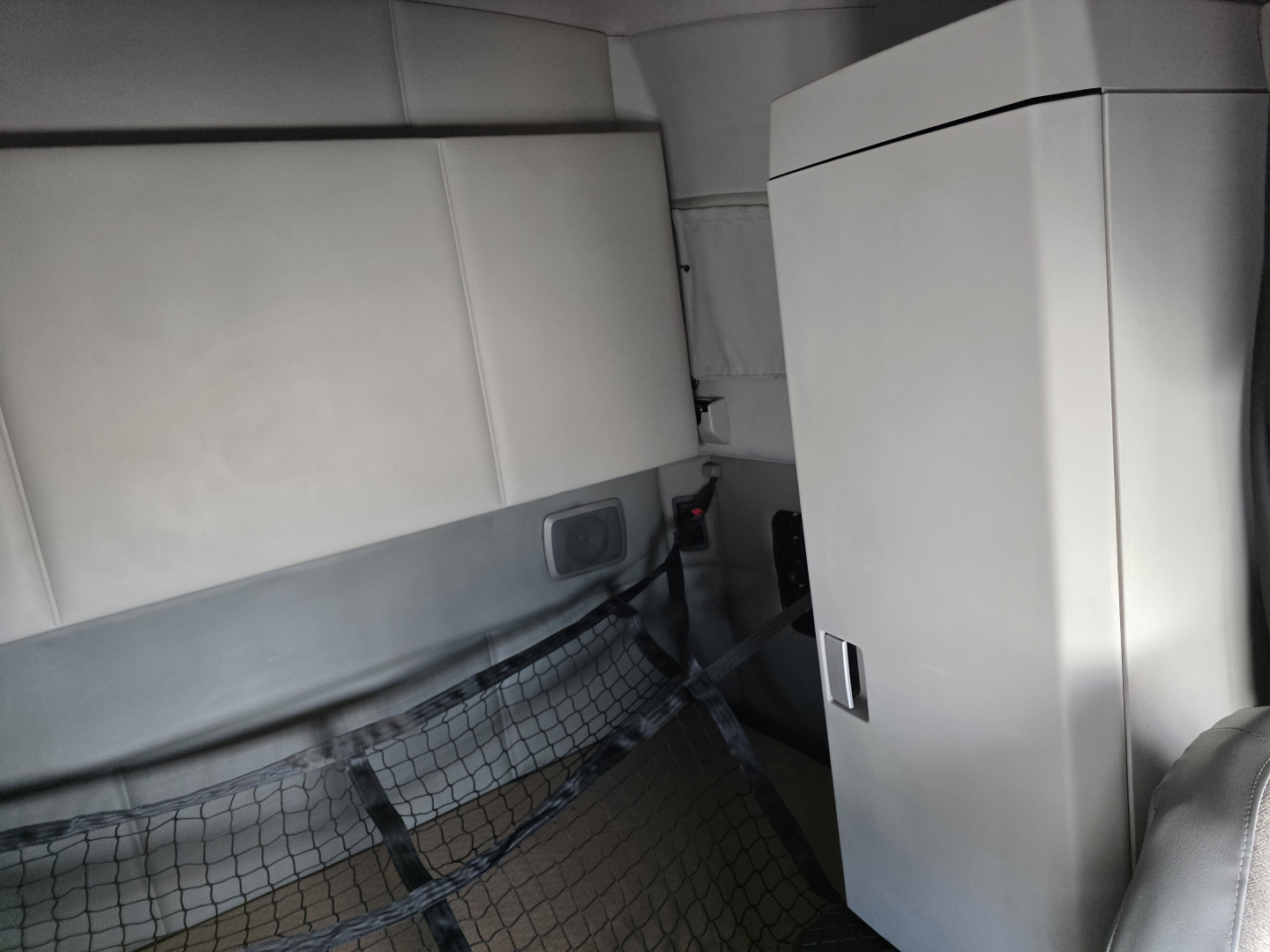 Interior view of a 2018 Kenworth T680 undercab area showing a vertical cabinet and cargo net, part of sleeper truck interior.