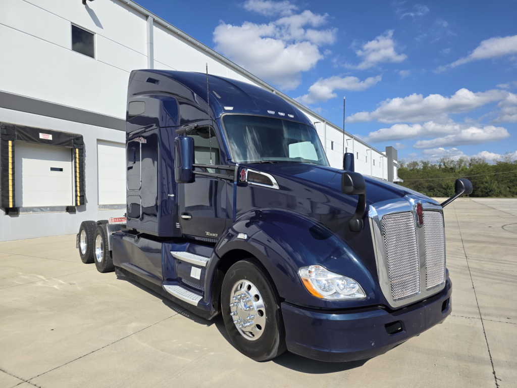 Kenworth T680 tractor-trailer cab in blue, front view, with chrome grille and dual rear axles visible.
