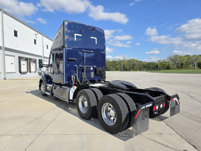 Kenworth T680 tractor with blue sleeper cab, rear view showing dual rear axles and mudflaps.