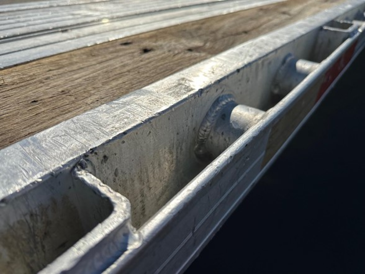 Trailer edge with wooden deck and metal frame showing tie-down cleats and channel cross-section.