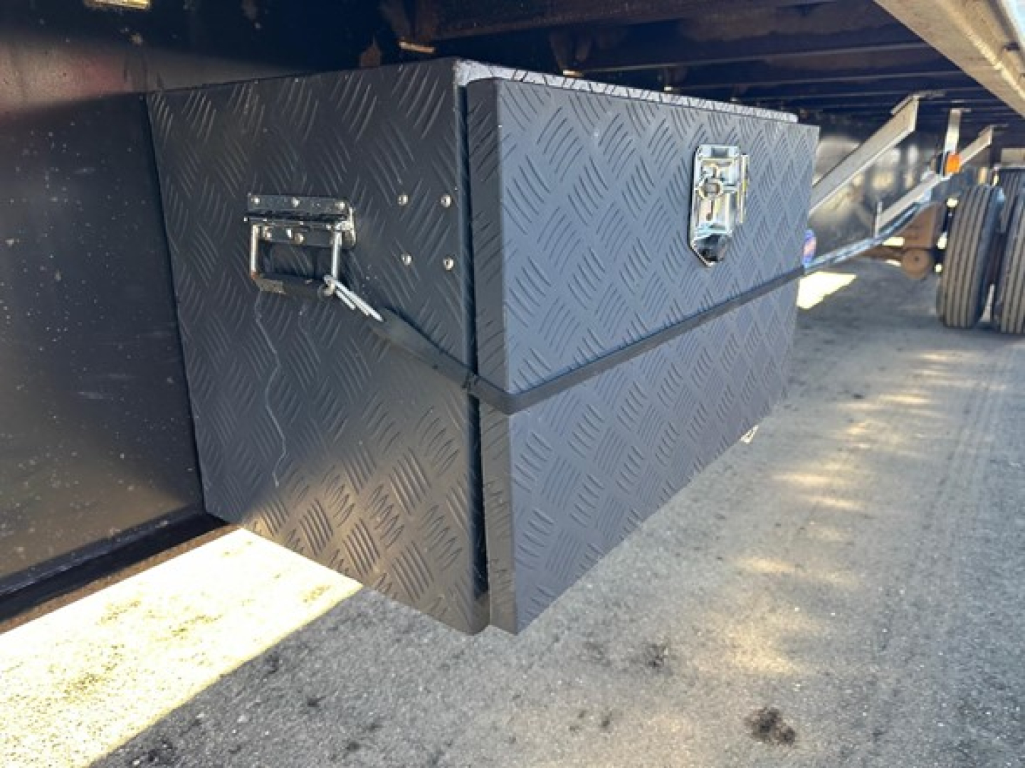 Flatbed trailer toolbox mounted underside showing diamond plate toolbox with latch and handles.