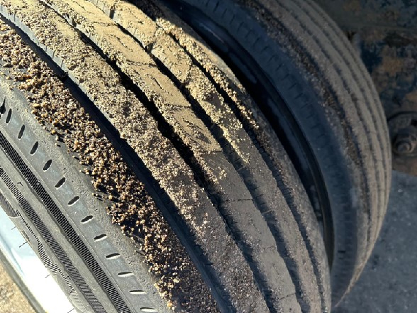 Tires of a used flatbed trailer showing tread and gravel on sidewall.