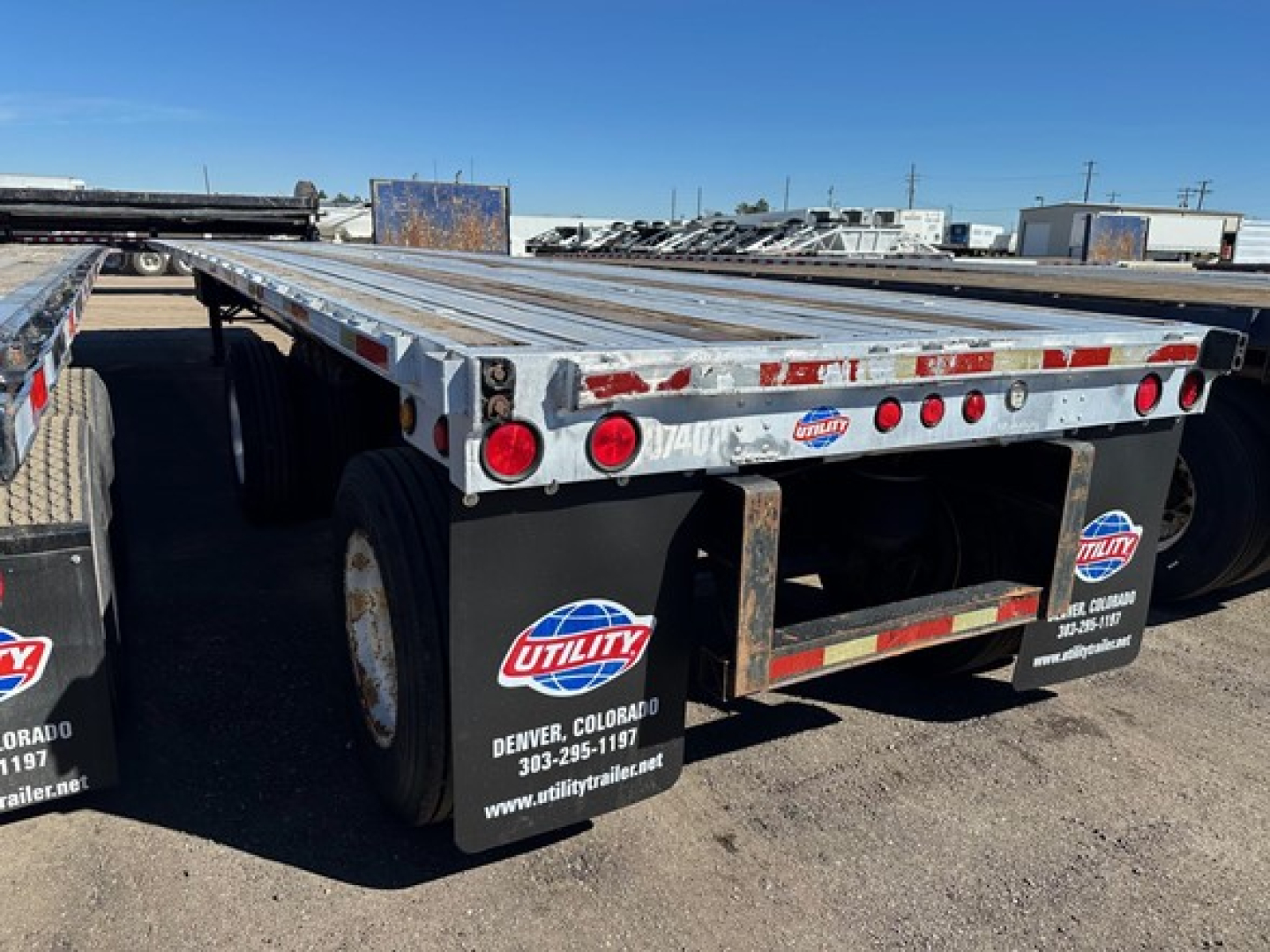 Flatbed trailer rear view showing aluminum deck, dual rear axles, UTILITY trailer mud flaps and logos