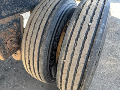 Twin wheel trailer axle showing dual tires with tread near the edge of a flatbed trailer.