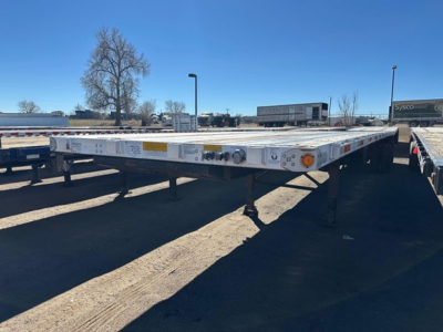 Flatbed trailer deck showing side markings and lights, utility spread air combo with adjustable legs in a used trailer lot.