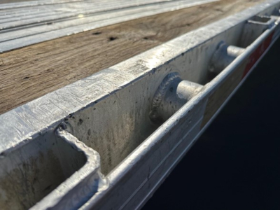 Trailer edge with wooden deck and metal frame showing tie-down cleats and channel cross-section.