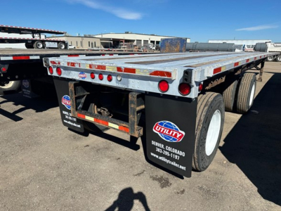Flatbed trailer showing Utility brand mud flaps and dual rear axles with reflective red/white tape along the sides and back; metal deck with wear; Denver, Colorado stickers on mud flaps.