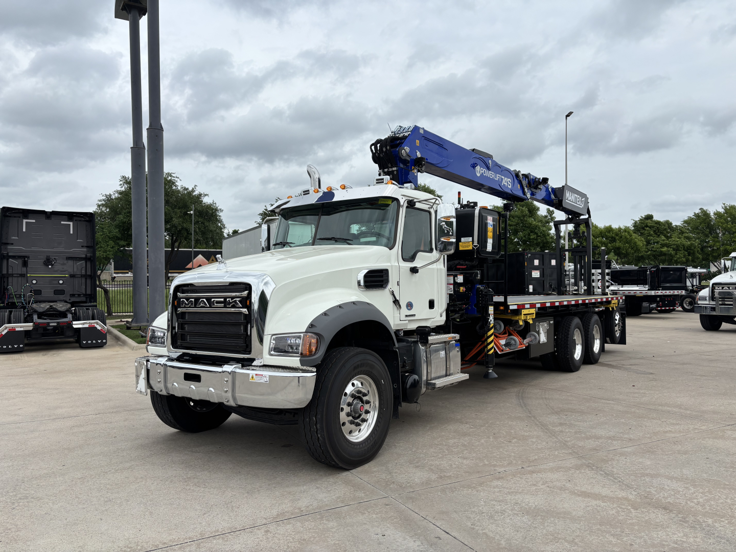 Truck in service with blue crane mounted on back, Mack GR64F model, white cab, crane arm extended overhead, flatbed equipment truck, VIN 1M2GR4GCXTM055964.