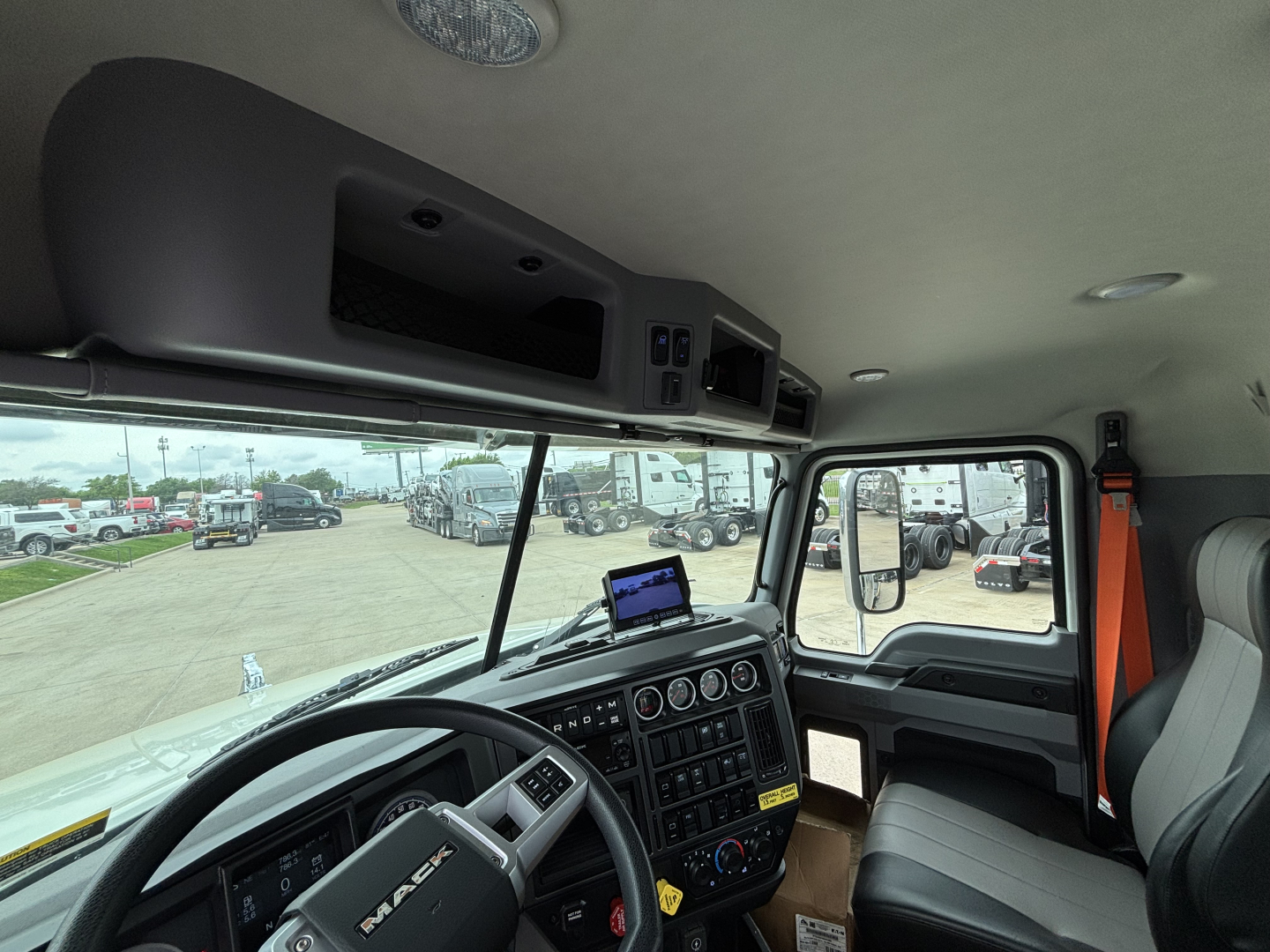 Interior view of a new Mack GR64F crane truck cab showing dashboard with multiple gauges, control panels, sun visor, mounted tablets, and passenger seat.