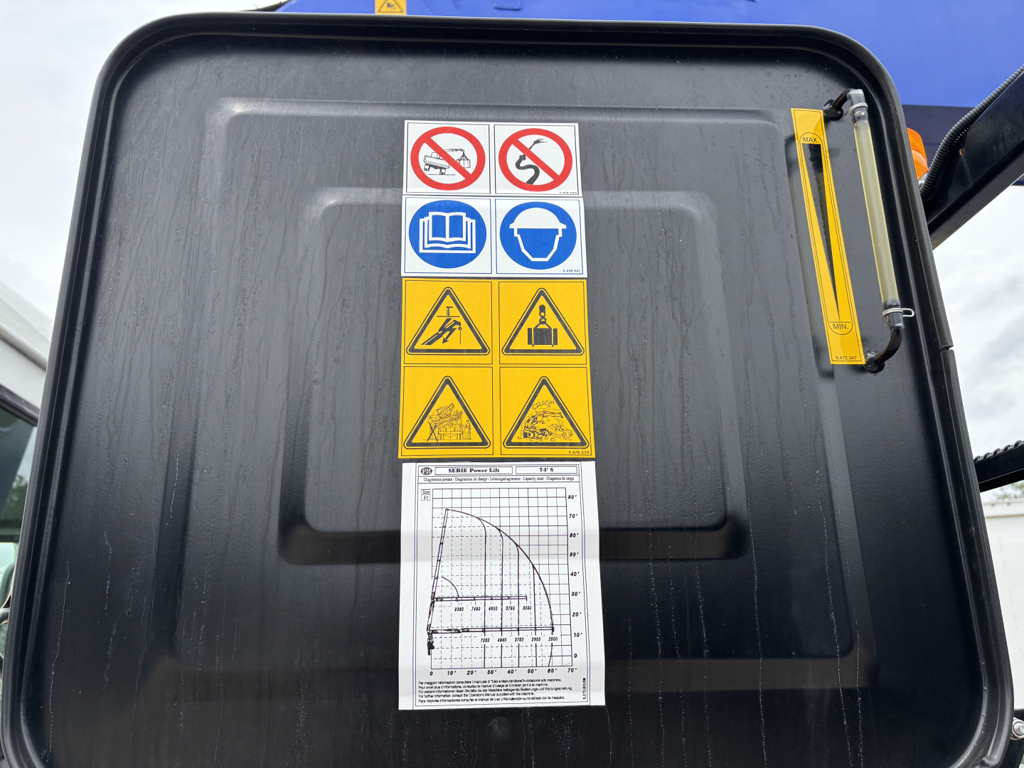 Mack GR64F crane cab door showing warning labels and a chart, with safety pictograms and a yellow ruler on the edge.