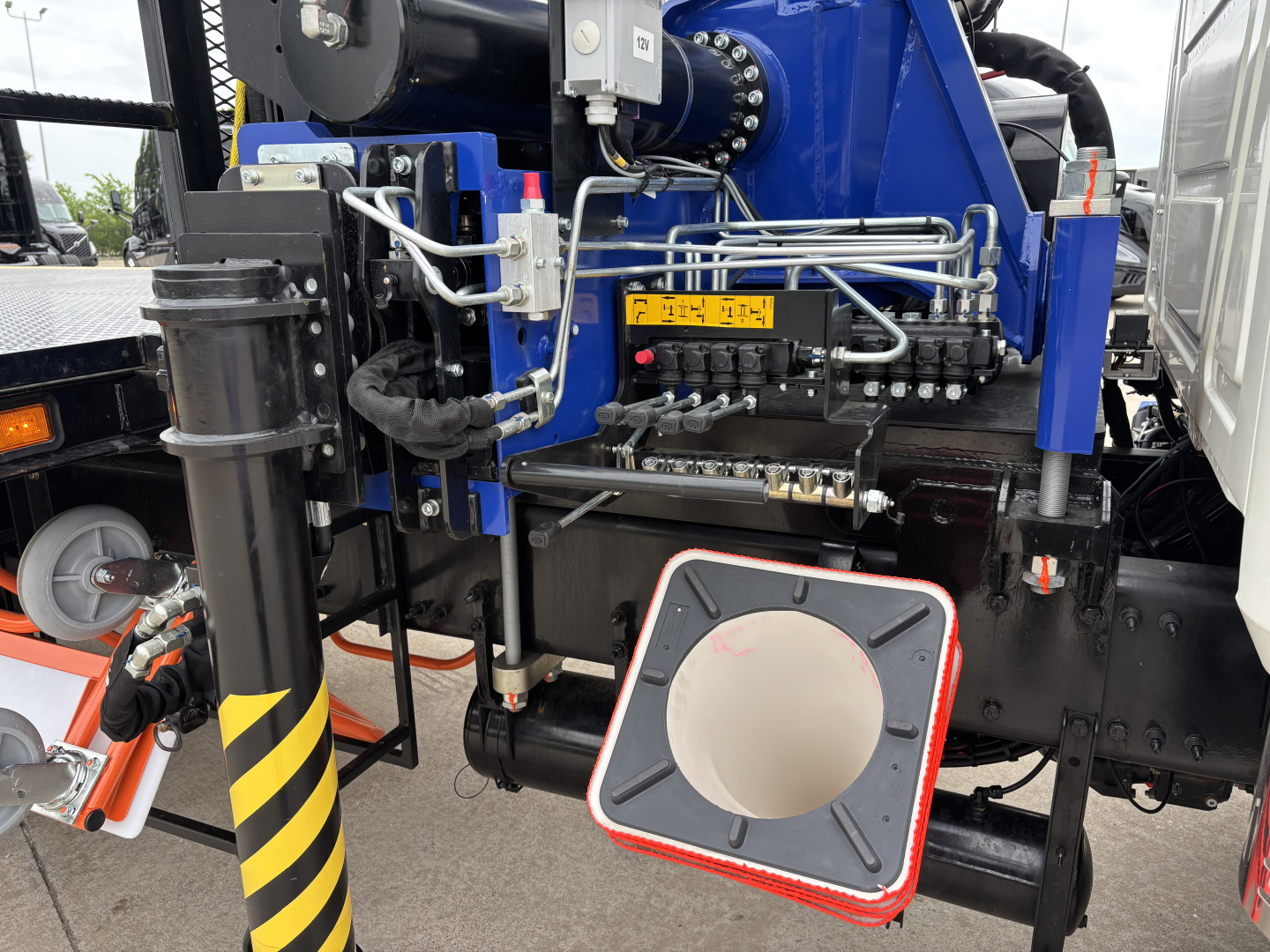 Mack GR64F crane truck showing hydraulic lines and operator controls with a circular inspection hatch and yellow label.