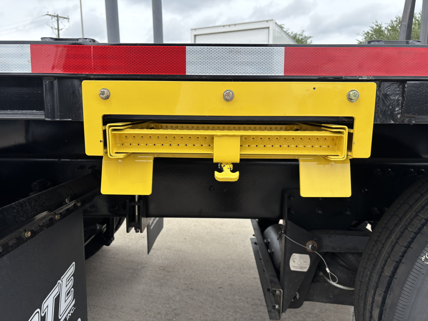 Rear view of a Mack GR64F truck chassis showing a bright yellow rear underride protection bar and hitch receiver assembly.