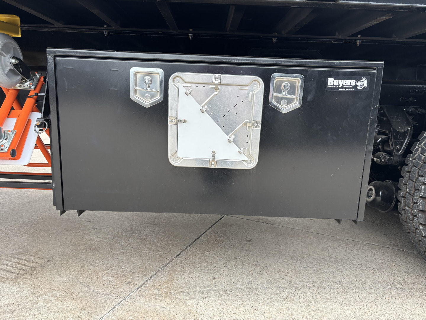 Toolbox mounted under a Mack GR64F truck with two latches and a central handle; Buyers equipment sticker visible on right side.