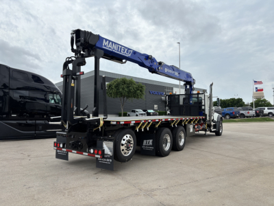 Mack GR64F crane truck in a dealership lot showing a blue Manitex crane arm and triple-axle trailer with black cab in background.