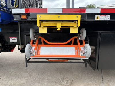 Truck crane carrier showing a yellow rear latch and orange underslung wheel rack with four wheels on a steel frame under the bed of a Mack GR64F crane truck.