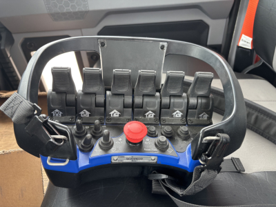 Control console with multiple levers and red emergency stop knob inside Mack GR64F crane cab showing eight switch levers and operator controls.